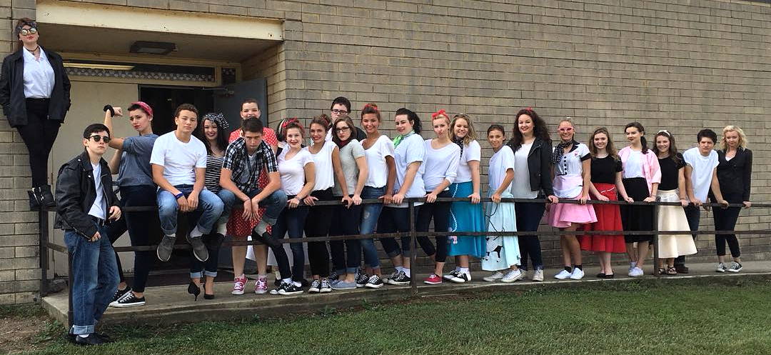 Een groep groep studenten van de Jackon County High Schools, poseert samen buiten een bakstenen gebouw. Sommigen staan, anderen zitten op een metalen reling.