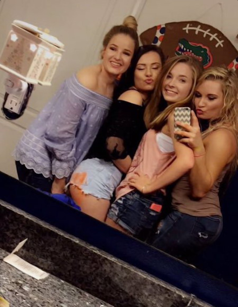 Vier high school studentes poseren samen voor een spiegelselfie in de badkamer. Ze lachen en trekken gekke bekken. Het zijn allemaal vriendinnen, die regelmatig op hun High School een stevig pak op hun billen krijgen. Het is goed te zien dat één meisje recent op haar billen heeft gekregen.Op de achtergrond is een muurdecoratie in de vorm van een voetbal te zien.