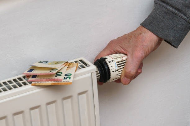 Een hand stelt een radiatorthermostaat af met eurobankbiljetten bovenop de radiator.