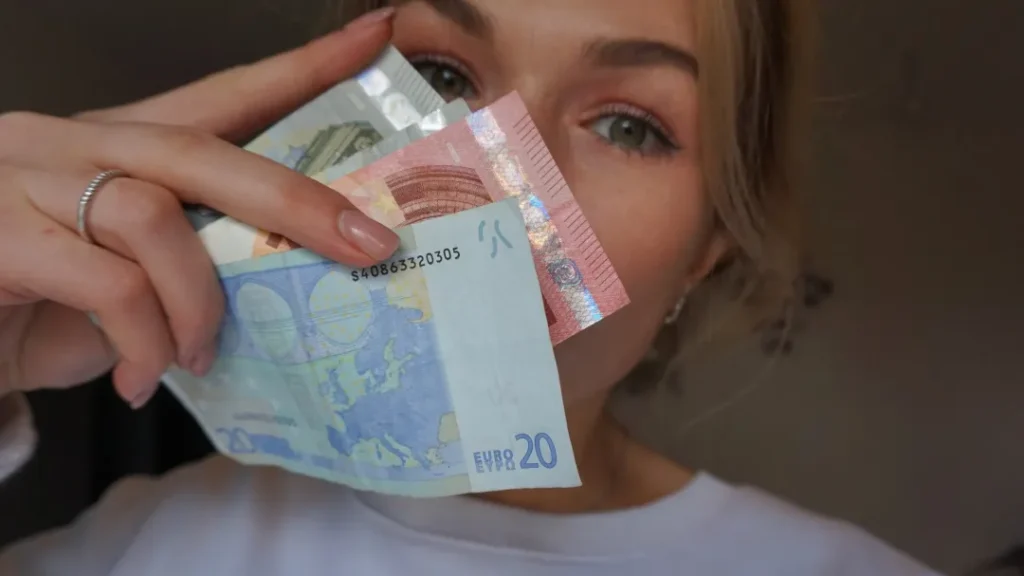 Een persoon die verschillende eurobiljetten voor zijn gezicht houdt, zijn mond gedeeltelijk bedekt en zijn ogen laat zien.