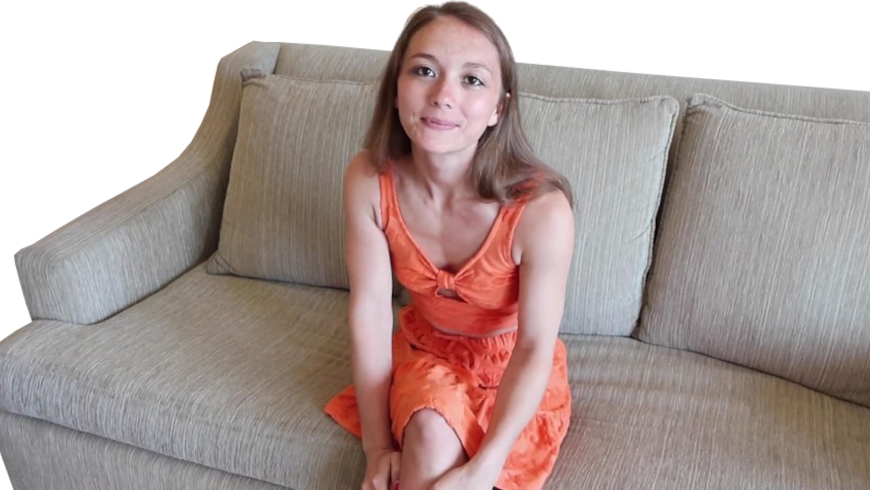 Een vrouw in een oranje jurk zit op een beige bank, kijkt met een lichte glimlach naar de camera en vangt een moment van aansluiting vinden temidden van eenzaamheid.