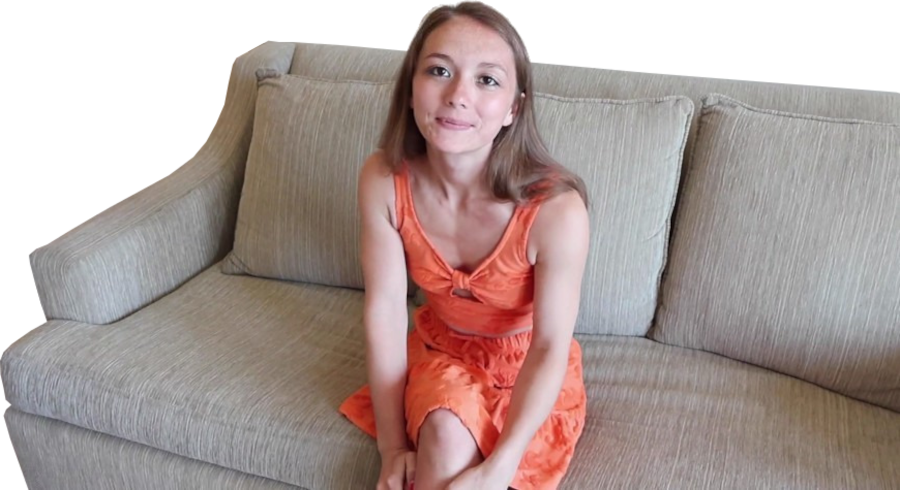 Een vrouw in een oranje jurk zit op een beige bank, kijkt met een lichte glimlach naar de camera en vangt een moment van aansluiting vinden temidden van eenzaamheid.