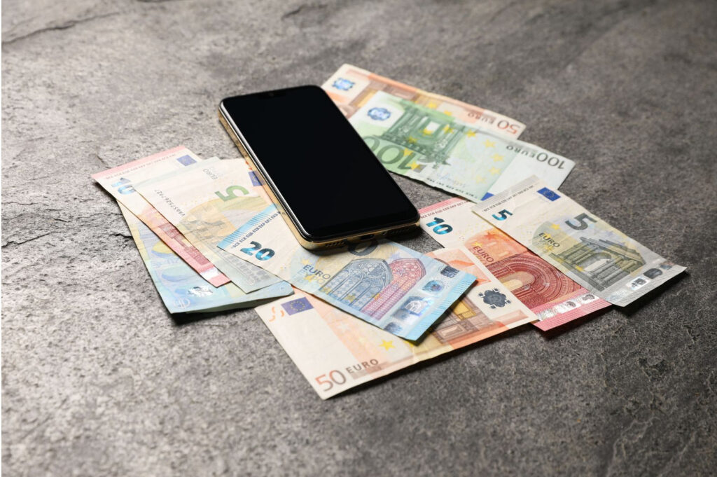 Een smartphone bovenop verschillende eurobankbiljetten op een grijs stenen oppervlak.