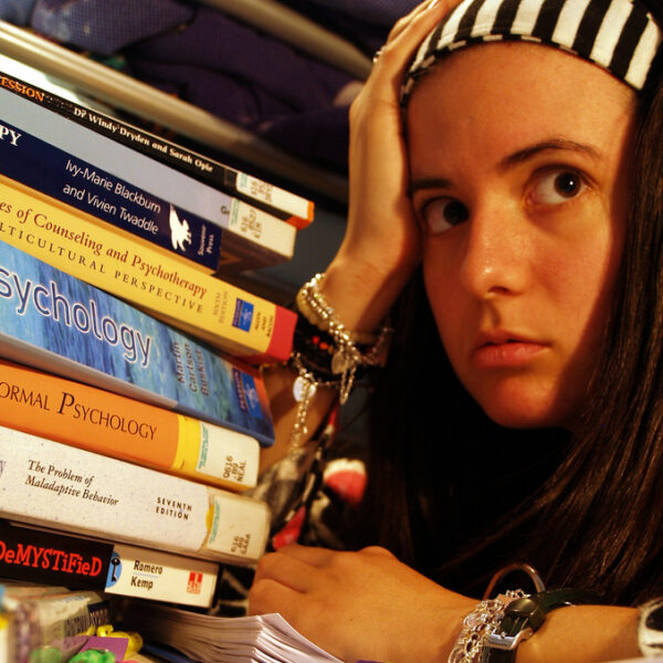 Een jongere met een gestreepte hoofdband kijkt gestrest terwijl hij naast een hoge stapel psychologie- en therapieboeken zit.