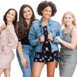 Zes jonge vrouwen staan op een rij en glimlachen naar de camera. Ze zijn gekleed in casual lente- of zomeroutfits tegen een effen, lichte achtergrond.