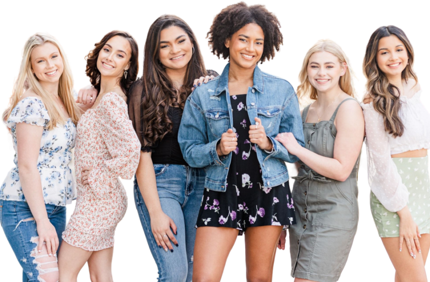 Zes jonge vrouwen staan op een rij en glimlachen naar de camera. Ze zijn gekleed in casual lente- of zomeroutfits tegen een effen, lichte achtergrond.